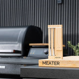 MEATER device on a table with a grill in the background