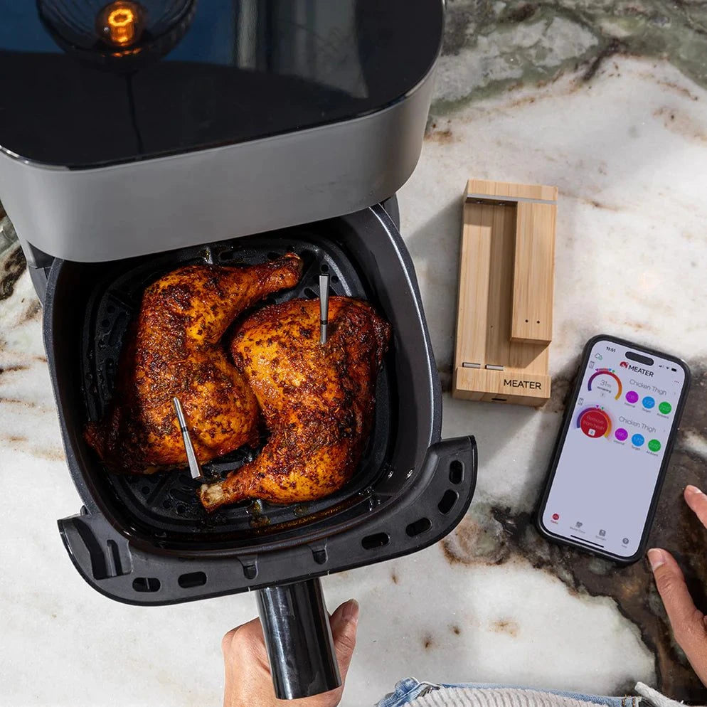 Air fryer with roasted chicken inside, smartphone app on marble surface using meater